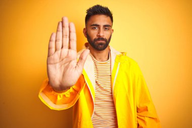 Sarı arka planda duran yağmurluk giyen genç Hintli adam avucunun içi gibi şarkı söylemeyi kesiyor. Yüzünde olumsuz ve ciddi bir jest olan uyarı ifadesi.