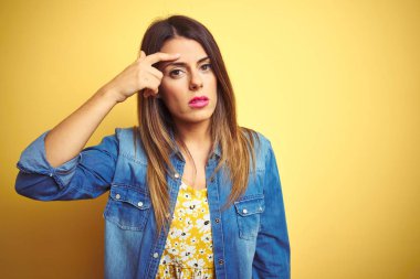 Sarı arka planda duran genç ve güzel bir kadın alnındaki sivilceden mutsuz olduğunu gösteriyor. Siyah noktalı çirkin bir enfeksiyon. Sivilce ve deri problemi