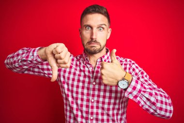 Genç ve yakışıklı bir adam, soyutlanmış kırmızı arka planda, baş parmaklarını kaldırıyor, anlaşmazlık ve uzlaşma ifadesi sergiliyor. Çılgın çatışma