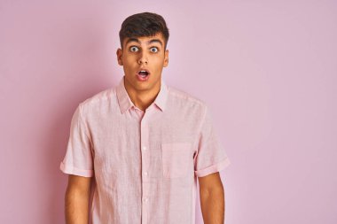 Izole pembe arka plan üzerinde duran rahat gömlek giyen genç hintli adam korkmuş ve sürpriz ifade ile şok, korku ve heyecanlı yüz.
