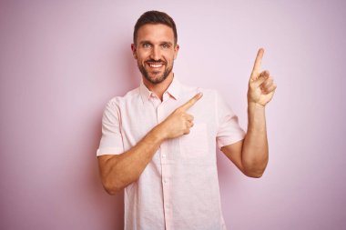 Pembe izole edilmiş arka planda zarif bir yaz gömleği giyen genç yakışıklı adam gülümseyip kameraya bakıyor ve iki eliyle ve parmaklarıyla kenarı işaret ediyor..