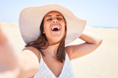 Genç ve güzel bir kadın mutlu bir şekilde gülümsüyor. Maspalomas Kumsalında akıllı telefon kullanarak selfie çekiyor.