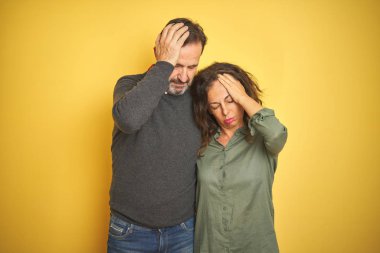 Güzel bir orta yaşlı çift, sarı arka planda acı ve migren yüzünden çaresiz ve stresli bir baş ağrısından muzdarip. Ellerini başının üstüne koy..