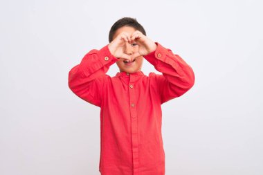 Zarif kırmızı tişört giyen güzel bir çocuk izole edilmiş beyaz arka planda duruyor. Sevgiyle gülümsüyor, elleriyle kalp sembolü yapıyor. Romantik konsept.