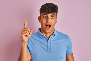 İzole edilmiş pembe arka planda duran mavi polo giyen genç Hintli adam başarılı bir fikri işaret ediyor. Heyecanlı ve mutlu. Bir numara..