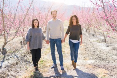 Üç neşeli yürüyüş toghether şeftali bahçesinde bahar güneşli gün zevk pembe yaprakları ile gülümseyen güzel aile