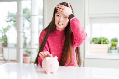 Güzel Asyalı kadın domuz çantasına bozuk para koyuyor elleri başının üstünde, utanç ve şaşkınlık dolu, sinirli ve hayal kırıklığına uğramış bir şekilde. Hata için korku ve üzüntü.