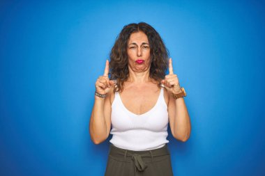 Kıvırcık saçlı orta yaşlı bir kadın mavi izole edilmiş arka planda dikiliyor üzgün ve üzgün görünüyor, parmaklarıyla yönü gösteriyor, mutsuz ve depresif..