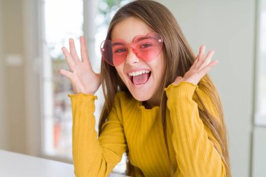 Pembe kalp gözlüğü takan güzel bir kız çocuğu çılgın ve başarıyı kolları açık ve gözleri açık heyecanla haykırarak kutluyor. Kazanan konsept