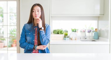 Çene düşünme hakkında soru, dalgın ifade üzerine el ile beyaz tabloda denim ceket giyen güzel Asyalı kadın. Düşünceli yüzüyle gülümsüyor. Şüphe kavramı.