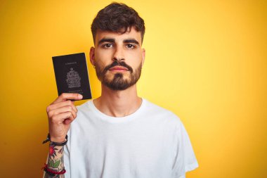 Kanada pasaportu takan dövmeli genç bir adam izole edilmiş sarı bir arka planı var. Akıllı bir yüz ifadesi var ve ciddi düşünüyor.