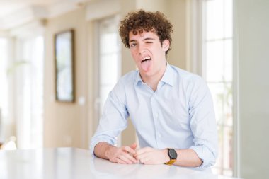 Kıvırcık saçlı genç iş adamı komik bir ifadeyle dilini dışarı çıkartıyor. Duygu kavramı.