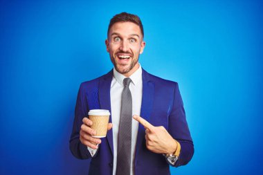Genç yakışıklı bir iş adamı mavi bir arka planda kahve içiyor. El ve parmağıyla işaret ederek çok mutlu.