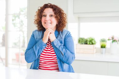 Orta yaşlı, kıvırcık saçlı, kot ceket giyen, gergin ve heyecanlı, çenesi yana bakan bir kadın.