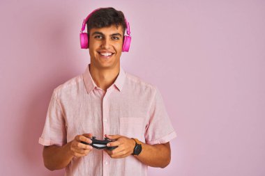 Hintli oyuncu video oyunu oynuyor. Pembe arka planda kulaklık takıyor. Gülümsüyor ve gülümsüyor.