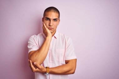 Pembe izole edilmiş arka plan üzerinde zarif gömlek giyen genç yakışıklı adam kollarını kavuşturarak depresyondan sıkılmış ve yorgun göründüğünü düşünüyor..
