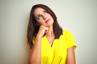Sarı tişört giyen genç güzel kadın beyaz izole arka plan üzerinde duran elleri çeneüzerinde soru, dalgın ifade düşünme. Düşünceli bir yüzle gülümsüyor. Şüphe kavramı.