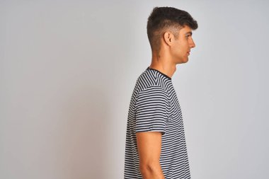 Genç Hintli adam, donanma çizgili tişört giyiyor. İzole edilmiş beyaz arka planda duruyor. Kendine güvenen bir gülümsemeyle rahat bir görünüm sergiliyor..