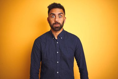 Genç ve yakışıklı Hintli işadamı, izole edilmiş sarı arka plan şişirme yanaklarının üzerine tişört giyiyor ve komik bir yüz takınıyor. Havayla şişmiş ağız, çılgın bir ifade..