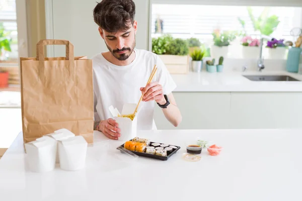 Young man eating sushi asian food and noodles using choopsticks