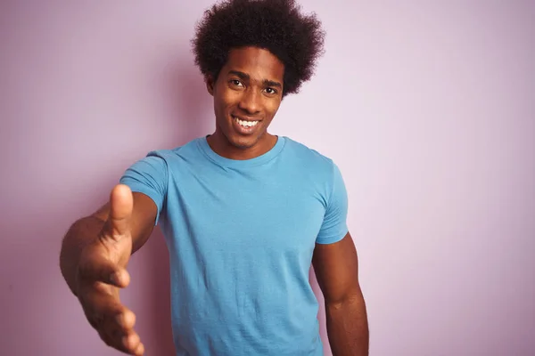 黑头发的非裔美国人穿着蓝色T恤 站在孤立的粉色背景上 微笑友好地握手致意和欢迎 成功的业务 — 图库照片