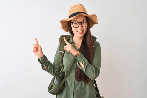 Chinese hiker woman wearing canteen hat glasses backpack over isolated white background smiling and looking at the camera pointing with two hands and fingers to the side.