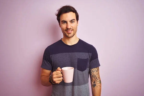 若いですハンサムな男とともに入れ墨コーヒーカップの孤立したピンクの背景に幸せな顔立ちと笑顔で自信を持って笑顔を示す歯 — ストック写真