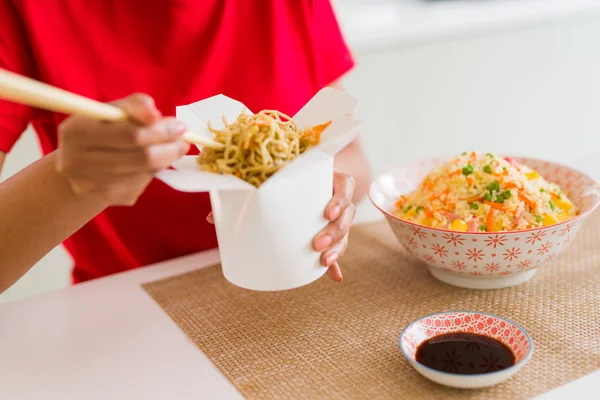 Primer plano de la mujer joven comiendo fideos de la caja de parto usando c —  Fotos de Stock