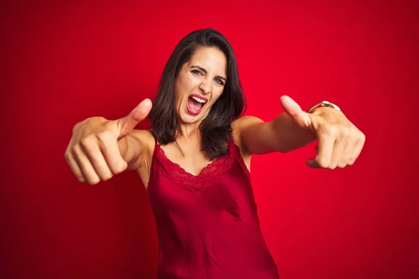 Young beautiful woman wearing sexy lingerie over red isolated background approving doing positive gesture with hand, thumbs up smiling and happy for success. Winner gesture.