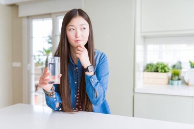 Güzel Asyalı kadın bir bardak tatlı su içiyor ciddi bir yüz sorgulamayı düşünüyor, kafası çok karışık bir fikir.