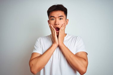 Asyalı genç bir Çinli tişört giyiyor. İzole edilmiş beyaz arka planda duruyor. Korkuyor ve şokta.