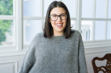 Güneşli bir günde evde rahat duran neşeli gülümseyen gözlüklü genç güzel kadın