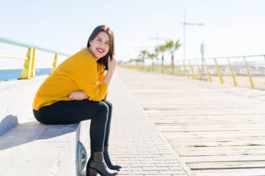 Güzel genç kadın bir mesire neşeli zevk güneş ışığı güneşli günde rahatlatıcı gülümseyen deniz kenarında oturup...