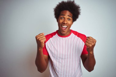 Afro saçlı, kırmızı çizgili tişörtlü, izole edilmiş beyaz arka plan üzerinde afro-amerikalı bir adam. Kollarını kaldırıp, açık gözlerle başarıyı kutluyor ve şaşırıyor. Kazanan konsept.