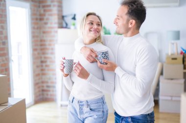 Genç güzel çift karton kutular etrafında yeni evde kahve fincan içme ayakta