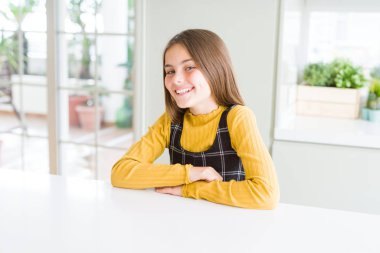 Güzel genç kız çocuk yüzünde mutlu ve güzel bir gülümseme ile masaya oturuyor. Şanslı kişi.