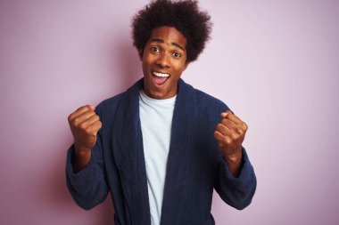 Genç Afro-Amerikalı bir adam pembe arka planda dikilip kollarını kaldırarak başarıyı kutluyor ve şaşırıyor. Kazanan konsept.