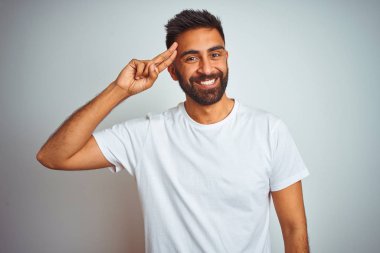 İzole edilmiş beyaz arka planda duran tişörtlü genç Hintli adam tek parmakla gülümseyerek, harika bir fikir ya da düşünceyle, iyi bir hafızayla,