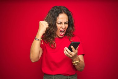 Orta yaşlı bir kadın kırmızı arka plan üzerinden akıllı telefon kullanıyor. Sinirli ve sinirli bir şekilde bağırıyor, çıldırıyor ve el kaldırarak bağırıyor.