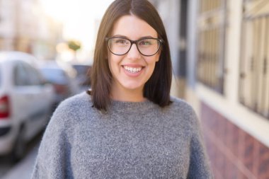 Genç güzel kadın gözlük giyerek şehir kasabasında sokakta emin yürüyüş gülümsüyor