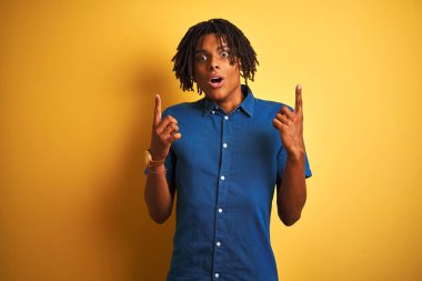 Rastgele kot gömlek giyen Afro adam izole edilmiş sarı arka planda dikilmiş şaşkın şaşkın bakıyor, parmaklarıyla işaret ediyor ve kollarını kaldırıyordu..