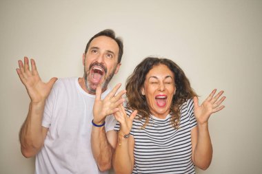 Güzel orta yaşlı çift, izole edilmiş beyaz arka planda ayakta durup başarının çılgınlığını kutlarken kollarını kaldırmış ve gözlerini kapatmış heyecanlı çığlıklar atıyorlar. Kazanan konsept