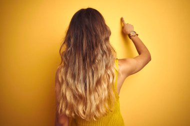 Sarı arka planda tişört giyen genç ve güzel bir kadın geriye doğru parmak eliyle poz veriyor.