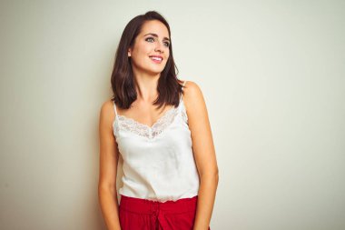 Beyaz izole arka plan üzerinde duran t-shirt giyen genç güzel kadın yüzünde gülümseme, doğal ifade ile yan bakıyor. Gülmekten emin.