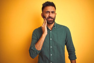 İnzivaya çekilmiş beyaz arka planda duran zarif bir gömlek giyen genç Hintli işadamı diş ağrısı ya da diş ağrısı yüzünden ağız ve acı dolu bir ifadeyle dokunuyor. Dişçi konsepti.