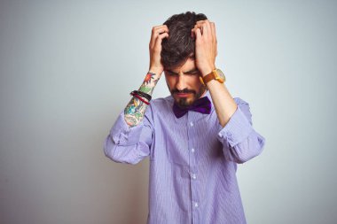 Mor gömlekli ve papyonlu genç adam izole edilmiş beyaz arka planda acı ve migren yüzünden çaresiz ve stresli bir baş ağrısı çekiyor. Ellerini başının üstüne koy..