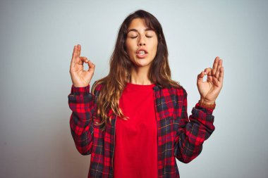 Kırmızı tişört ve ceket giyen genç ve güzel bir kadın beyaz izole arka planda duruyor rahatla ve gözleri kapalı gülümse parmaklarıyla meditasyon hareketi yapıyor. Yoga konsepti.