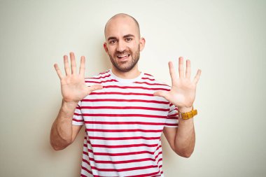 Sakallı, beyaz izole edilmiş arka plan üzerine normal çizgili kırmızı tişört giyen genç kel bir adam on numarayı gösterirken kendinden emin ve mutlu bir şekilde gülümsüyor..