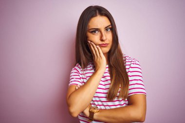 Çizgili tişört giyen genç ve güzel bir kadın izole edilmiş pembe arka planda dikilirken kolları çapraz olan depresyondan sıkılmış ve yorgun görünüyor..