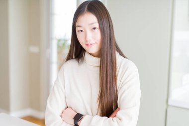 Rahat kazak giyen güzel Asyalı kadın yüzünde ciddi ifade ile rahat. Çapraz kollarla basit ve doğal